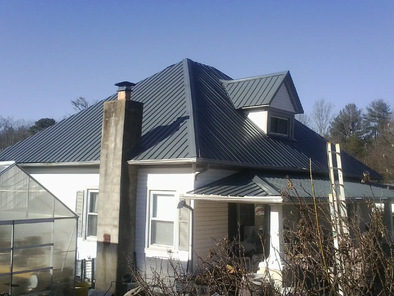 Dark blue standing seam metal roof on a white farmhouse with dormer — Slate & Tile Roof Repair by Roofing Brothers in New Hampton