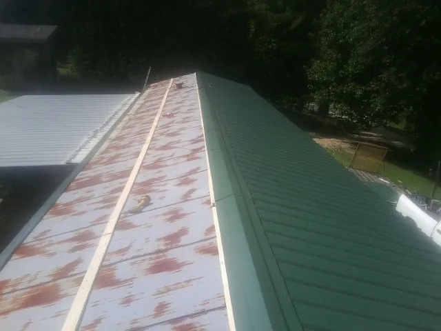 Old rusted panels beside newly installed green metal roofing — Wind Damage Roof Repair by Roofing Brothers in New Hampton