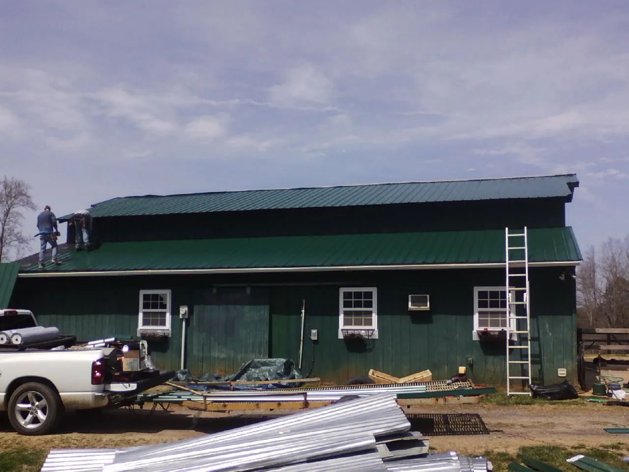 Crew installing green metal roofing on a large green barn in New Hampton