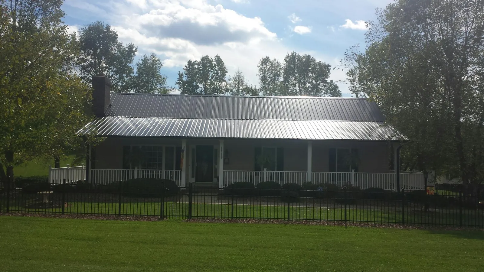 Gray metal roof on a brick ranch with a full width front porch — Gutter Guard Installation work by our crew in New Hampton